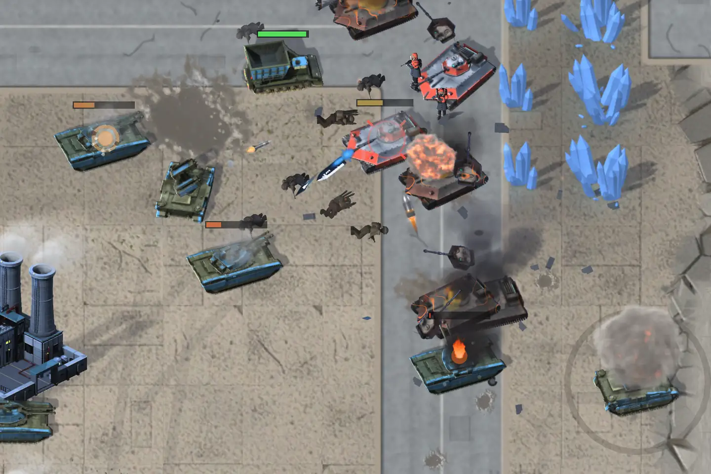 Two armies meet at a city crossroads, seen from above. Olive tanks with blue trim cross a lot of cracked paving from the left, past a power plant with twin stacks; on the road, white tanks with red armour plates and red-suited infantry push back, a blast blooms on one of them, and burning hulks smoke along the road. Pale blue crystals glitter at the upper right.