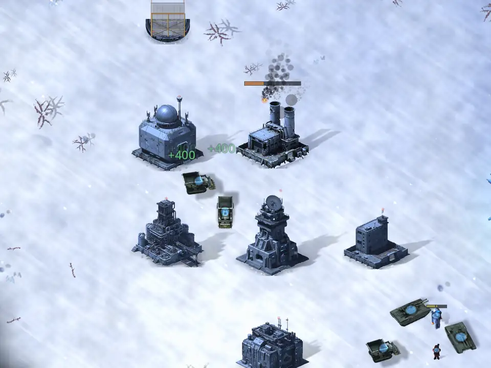 A base seen from above on deep snow: a white field with blowing snow streaking across it and bare dead shrubs poking through. One building is burning with an orange health bar over it, green +400 markers float where a truck has just unloaded, and two tanks and a soldier stand at the lower right.